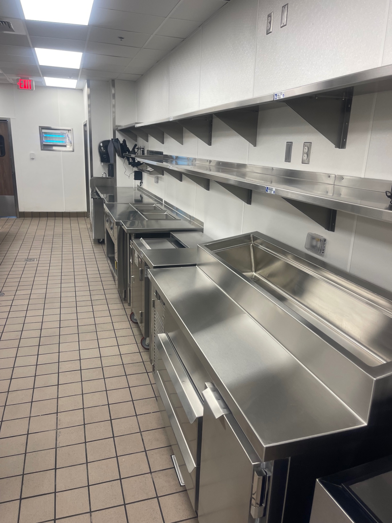 Stainless prep counters and overhead shelving along the kitchen wall after cleaning