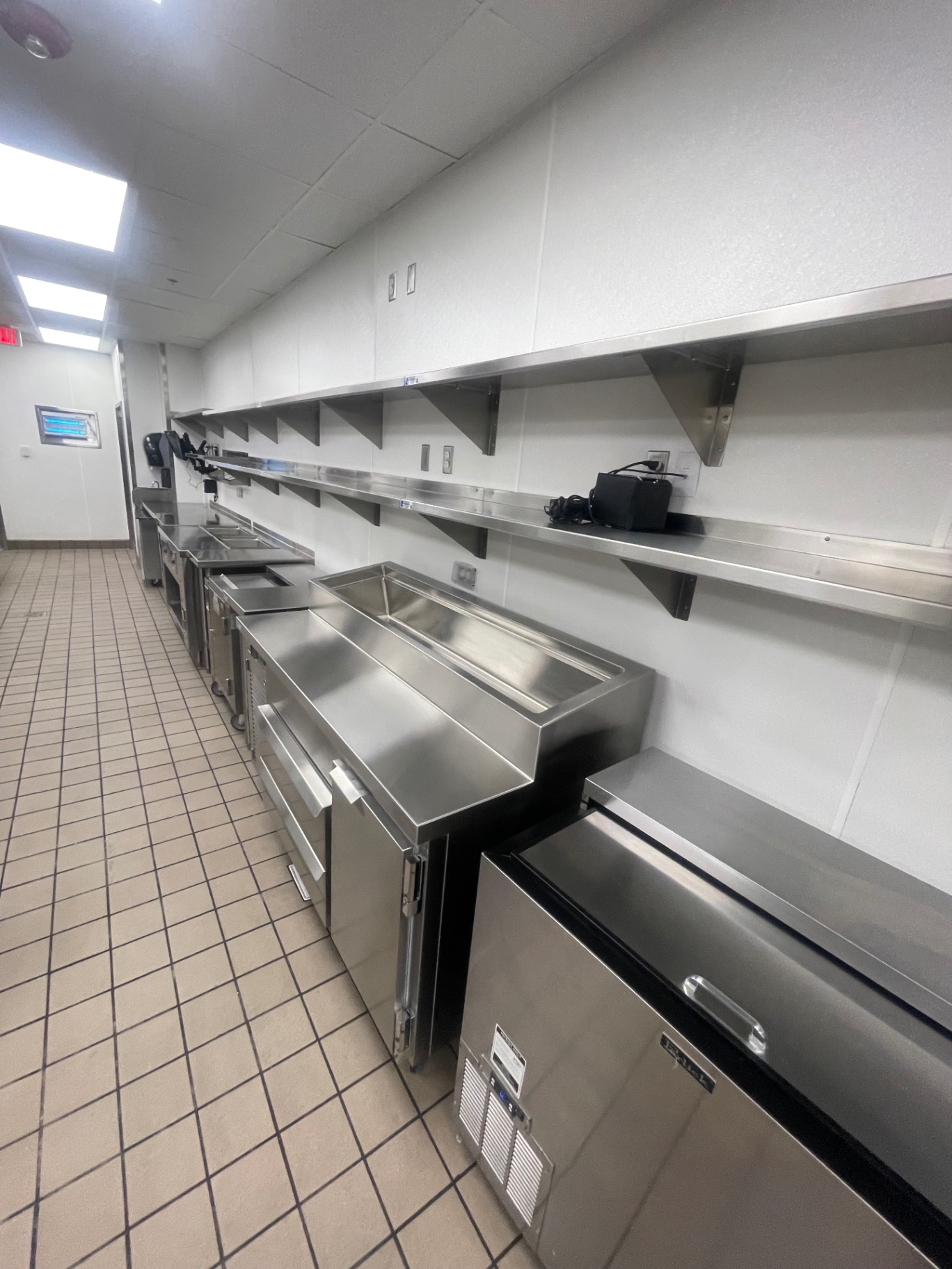 Cleaned stainless dish and prep line with wall shelving in the commercial kitchen